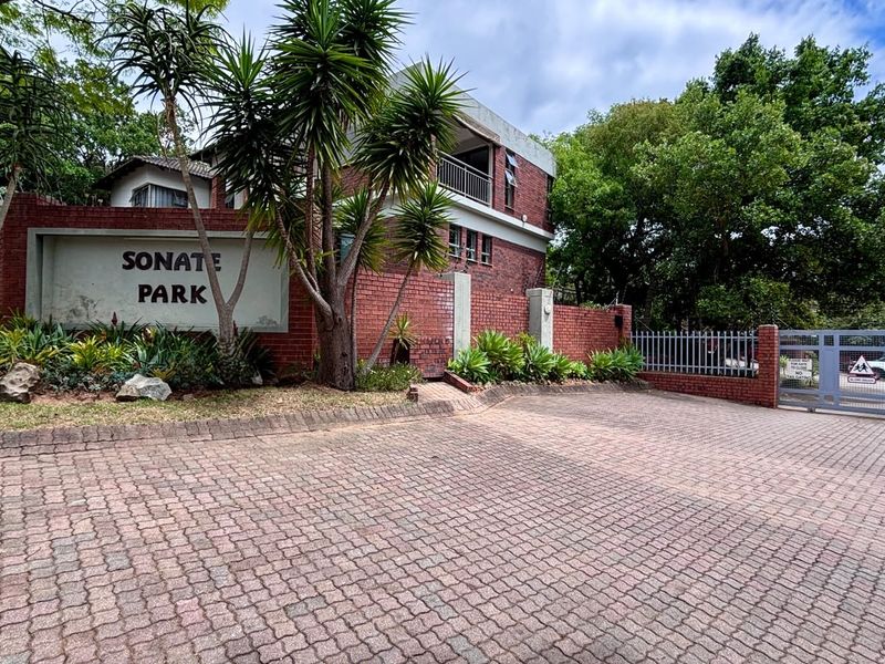 Front entrance view of Sonate Park complex featuring a paved driveway, brick boundary wall, and secure metal gate access.