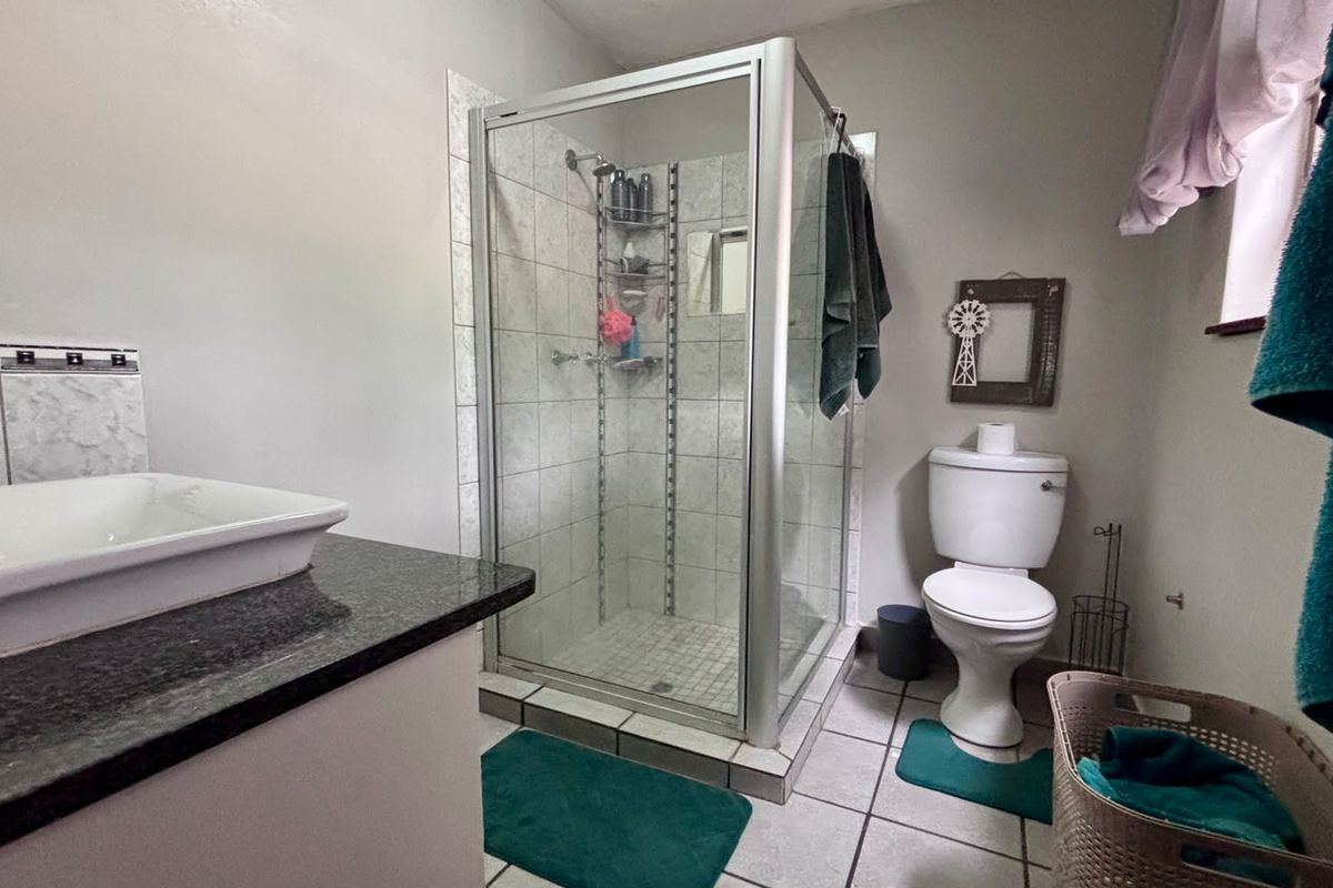 A functional bathroom featuring a corner shower enclosure, a white toilet, and a vanity basin set into a granite countertop with tiled flooring.