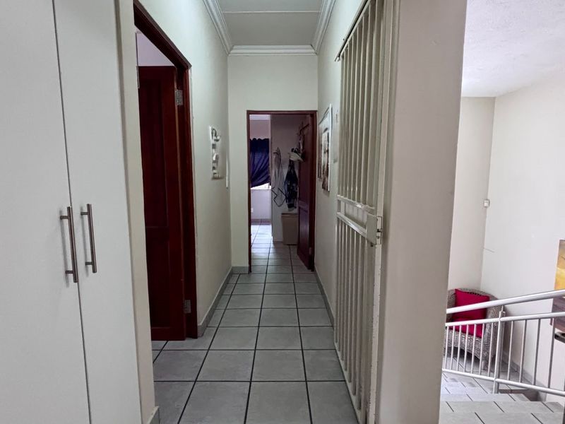 A functional hallway featuring tiled flooring, built-in storage cupboards, and a security gate, providing access to adjacent rooms and the staircase.