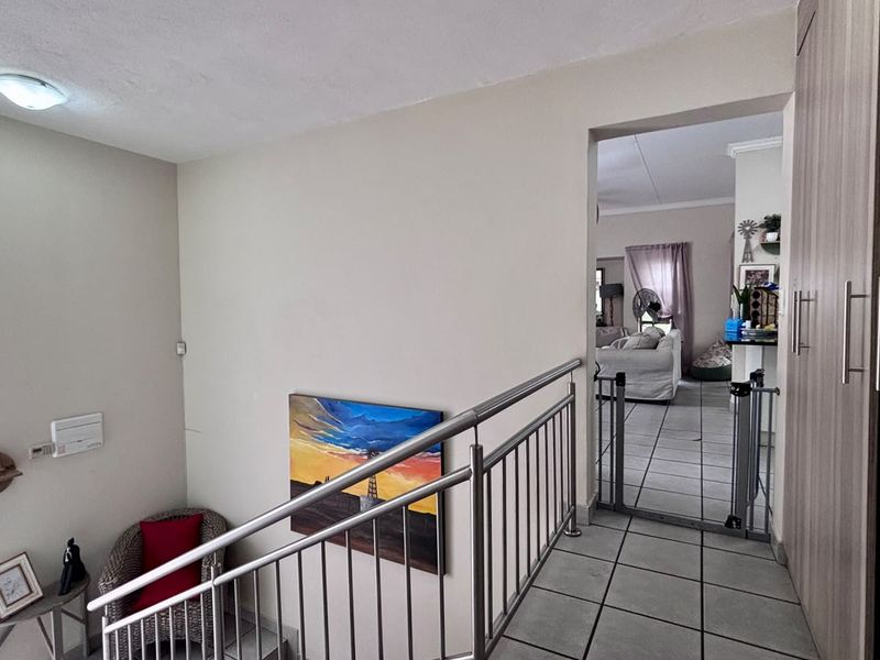 A bright hallway featuring tiled flooring, a modern stainless steel balustrade, and built-in storage cupboards, providing access to the adjacent living area.