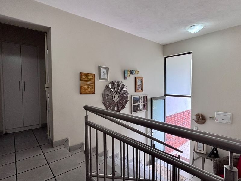 A bright hallway featuring a metal balustrade staircase, tiled flooring, and a built-in cupboard, providing access to upper-level living spaces.