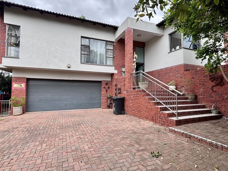 Front elevation of a two-story house featuring a brick facade, paved driveway, integrated garage, and a staircase leading to the main entrance.