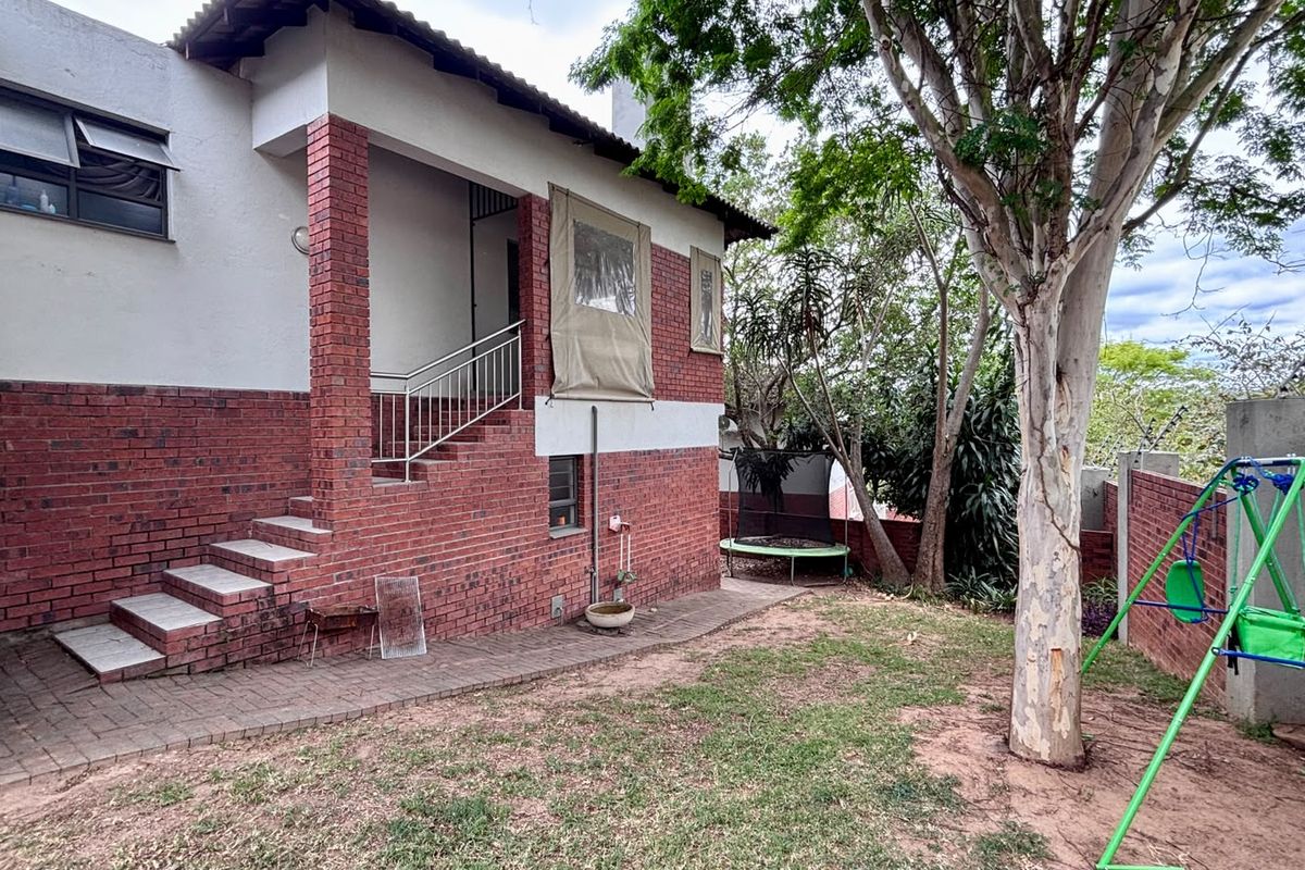Rear exterior view of the house featuring a brick facade, staircase with metal railing, paved walkway, and a garden area with boundary wall.