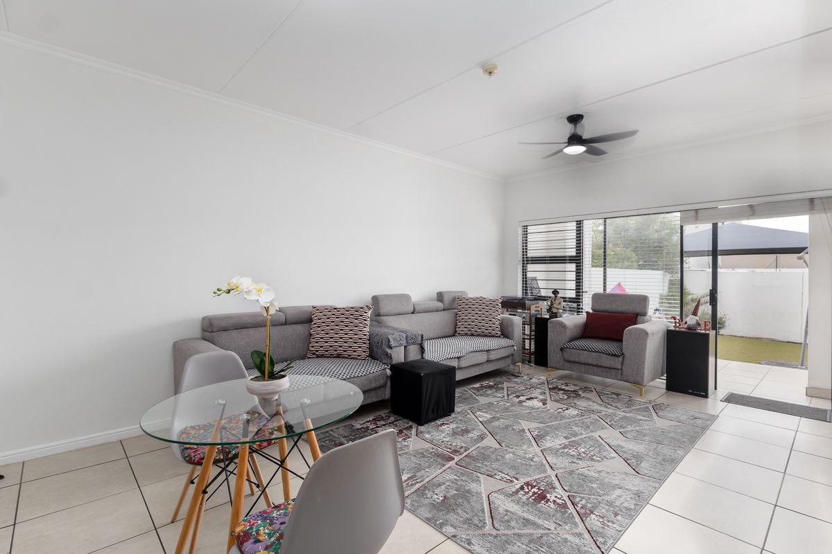 A bright living room featuring tiled flooring, a ceiling fan, and a large sliding glass door providing access to the outdoor area.