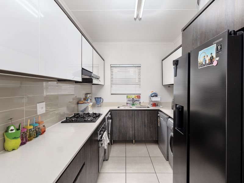 Modern galley-style kitchen featuring sleek white and dark wood cabinetry, stone countertops, gas hob, built-in oven, and tiled flooring.