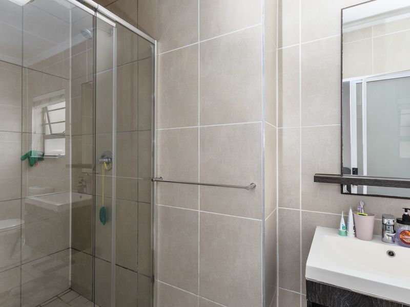 A modern bathroom featuring a glass-enclosed shower, neutral ceramic wall tiling, a vanity basin, and a wall-mounted mirror.