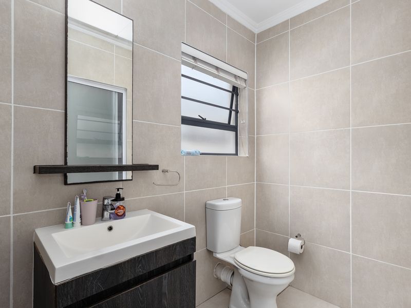 A modern, well-maintained bathroom featuring neutral wall tiles, a contemporary vanity cabinet with a basin, and a functional louvered window.
