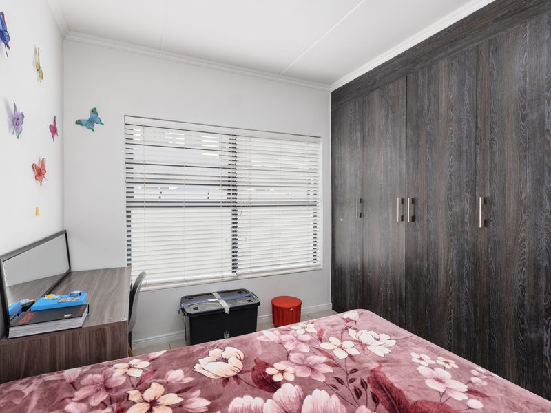 A well-maintained bedroom featuring dark wood-grain built-in cupboards, tiled flooring, and venetian blinds for privacy.
