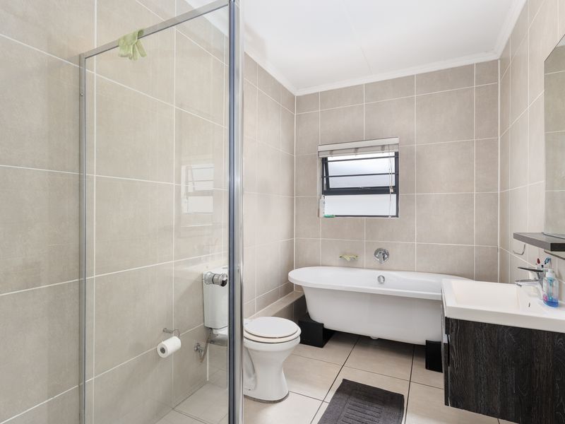 Modern bathroom featuring a freestanding bathtub, glass-enclosed shower, wall-mounted toilet, and a sleek vanity cabinet with neutral floor-to-ceiling tiling.