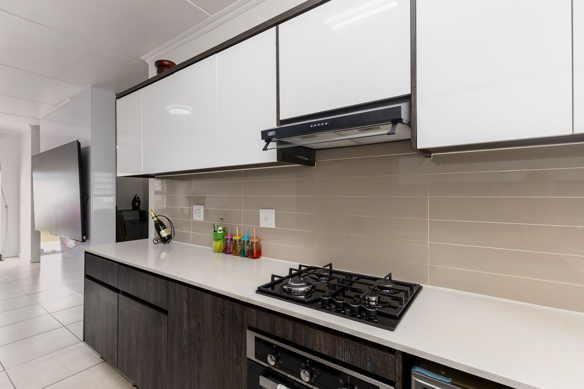 Modern kitchen featuring sleek two-tone cabinetry, stone countertops, a gas hob, and a built-in oven with a tiled backsplash.