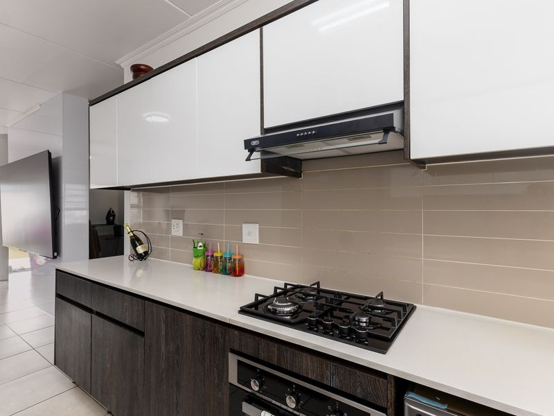 Modern kitchen featuring sleek two-tone cabinetry, stone countertops, a gas hob, and a built-in oven with a tiled backsplash.