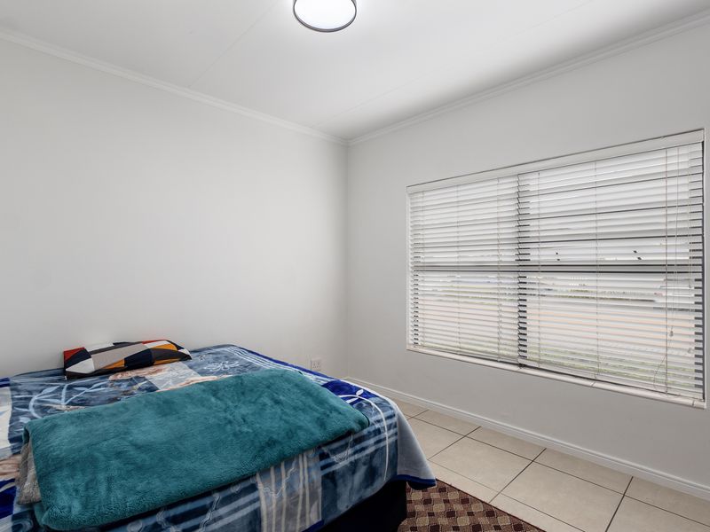 A clean and bright bedroom featuring neutral tiled flooring, a large window with fitted venetian blinds, and simple ceiling lighting.