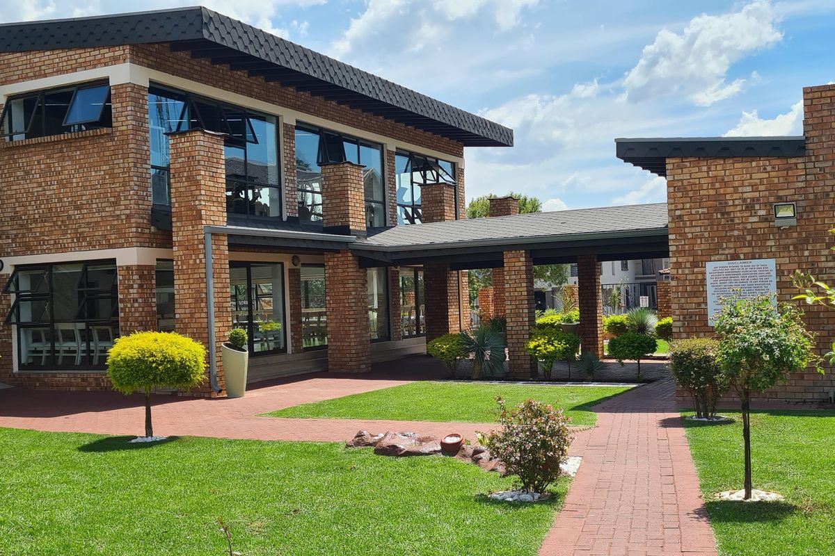 A well-maintained exterior view of a brick-faced building complex featuring a covered walkway, landscaped garden, and paved pathways.