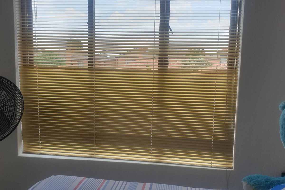 A bedroom featuring a large window with fitted horizontal blinds, providing natural light and a view of the surrounding residential area.