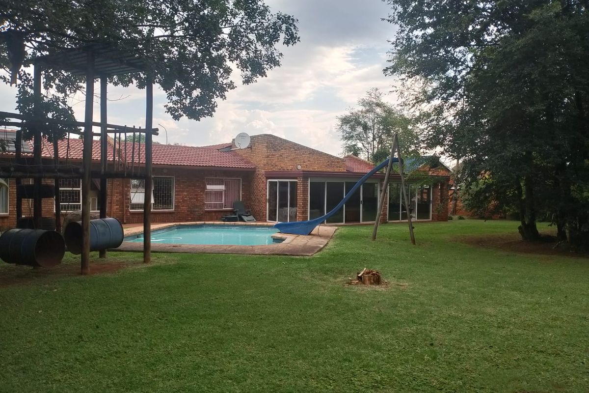 Spacious rear garden featuring a swimming pool, brick-faced house exterior, and integrated children's play equipment set within a mature, tree-lined yard.