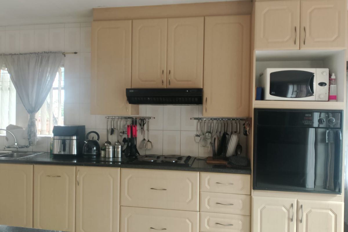 A functional kitchen featuring light-toned cabinetry, a built-in oven, a gas hob with an extractor fan, and dark granite countertops.