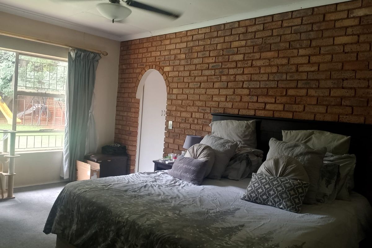 Spacious bedroom featuring a distinctive exposed brick feature wall, arched doorway, and large window providing natural light and garden views.