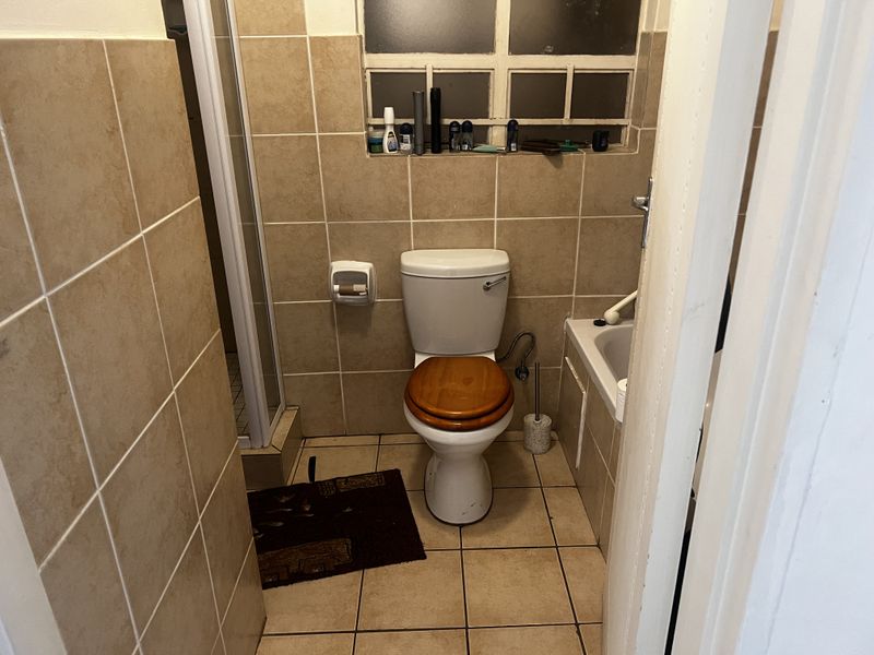A compact bathroom featuring a toilet, a bathtub, and a separate shower enclosure with neutral wall and floor tiling.