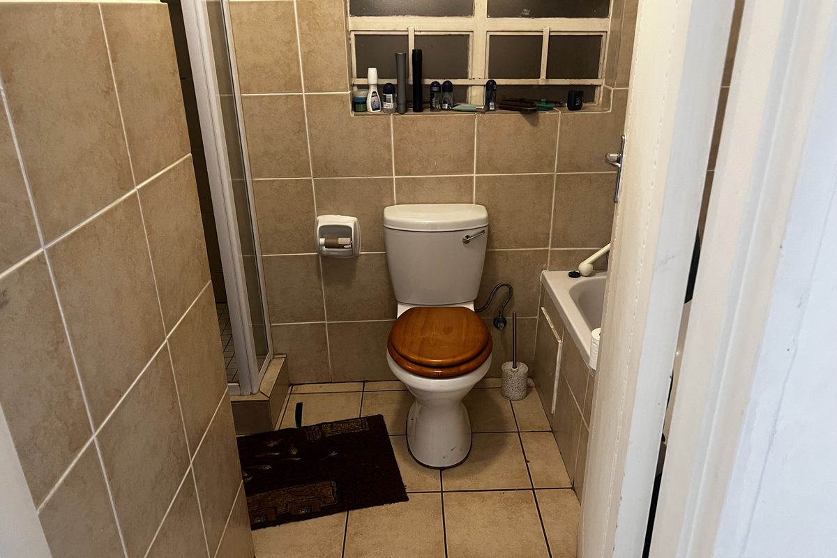 A compact bathroom featuring a toilet, a bathtub, and a separate shower enclosure with neutral wall and floor tiling.