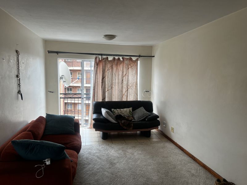 A living room area featuring a sliding glass door leading to a small balcony, with neutral wall finishes and carpeted flooring.