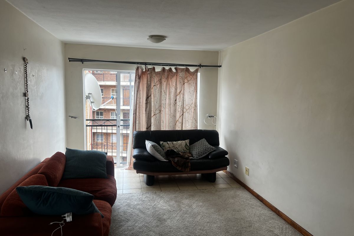 A living room area featuring a sliding glass door leading to a small balcony, with neutral wall finishes and carpeted flooring.