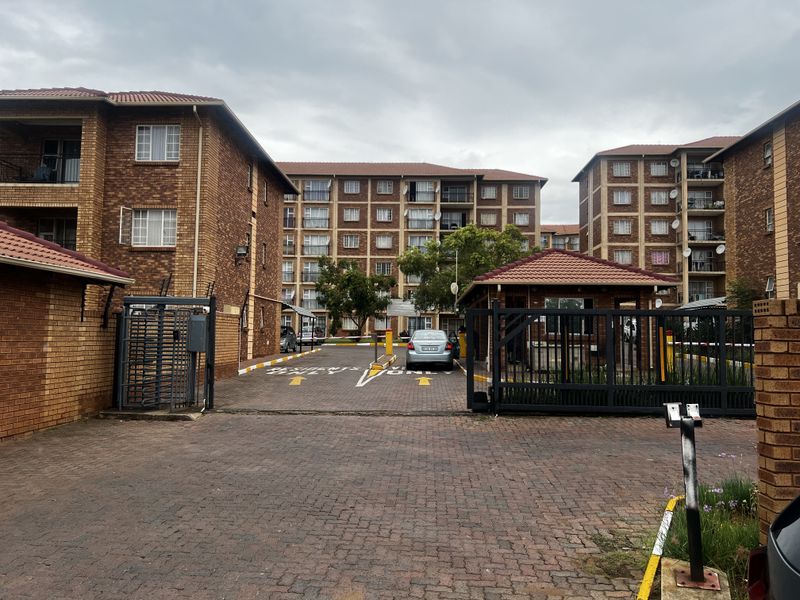View of the apartment complex entrance featuring brick facade buildings, paved driveway, and secure gated access point.