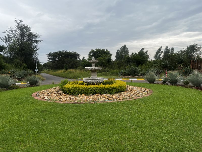A landscaped roundabout featuring a central stone fountain, manicured lawn, and decorative rock border within a residential estate setting.