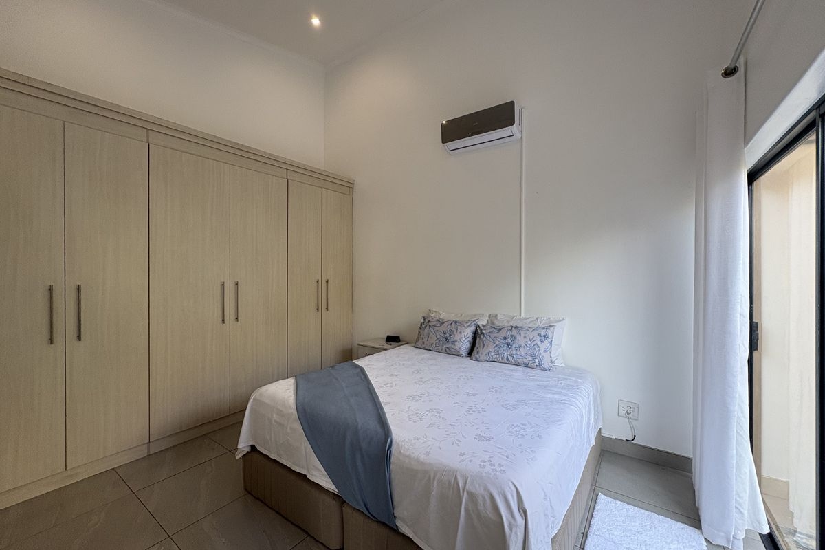 A well-maintained bedroom featuring built-in wooden cabinetry, tiled flooring, and a wall-mounted air conditioning unit with direct access to an outdoor area.