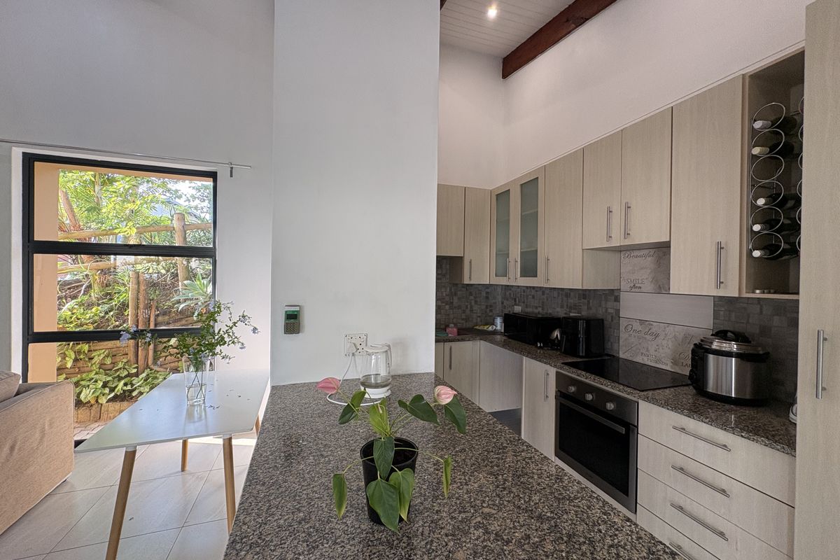 Modern kitchen featuring granite countertops, light wood cabinetry, built-in oven and hob, and high vaulted ceilings with exposed timber beams.