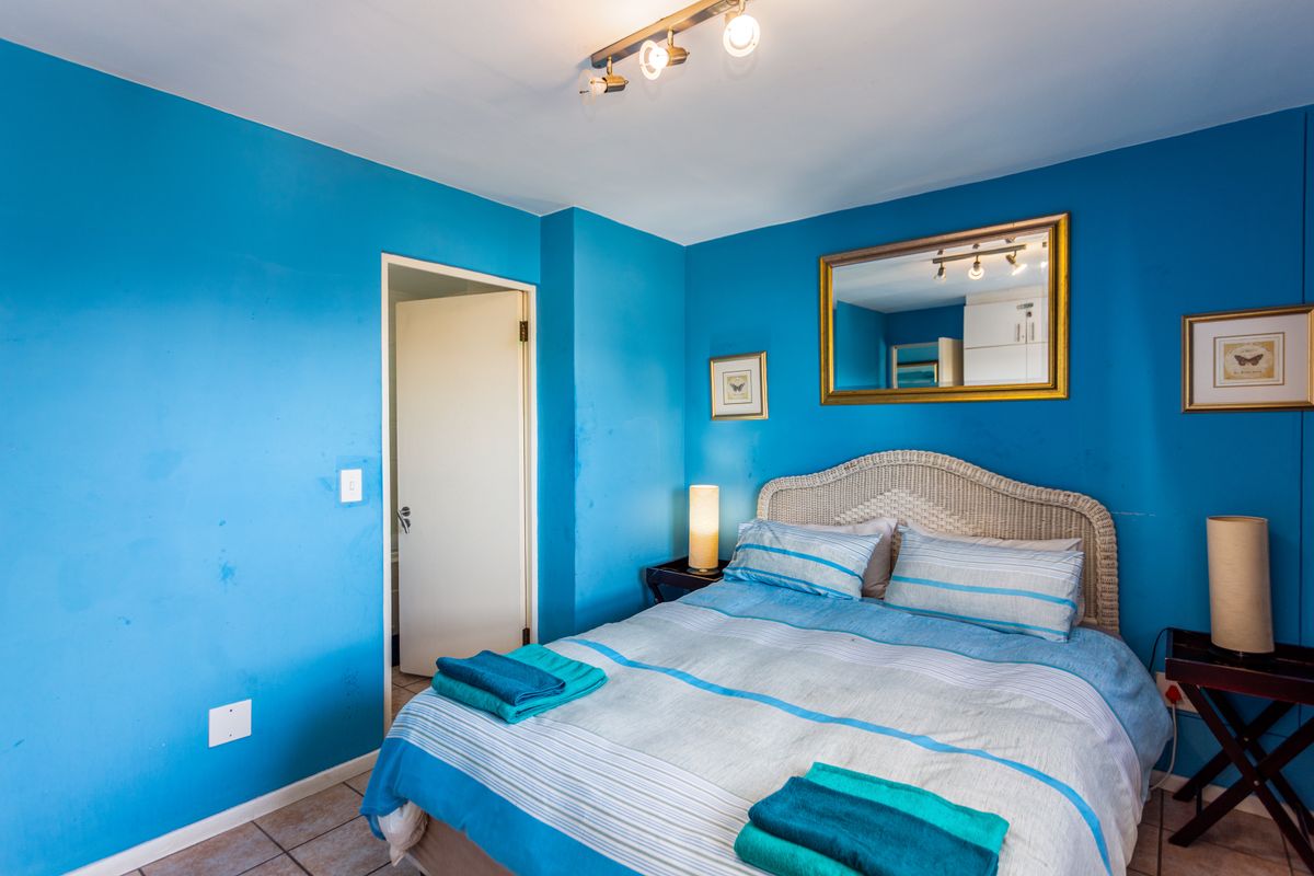 A bedroom featuring bright blue walls, tiled flooring, and a ceiling-mounted spotlight fixture, with an adjacent doorway leading to another room.