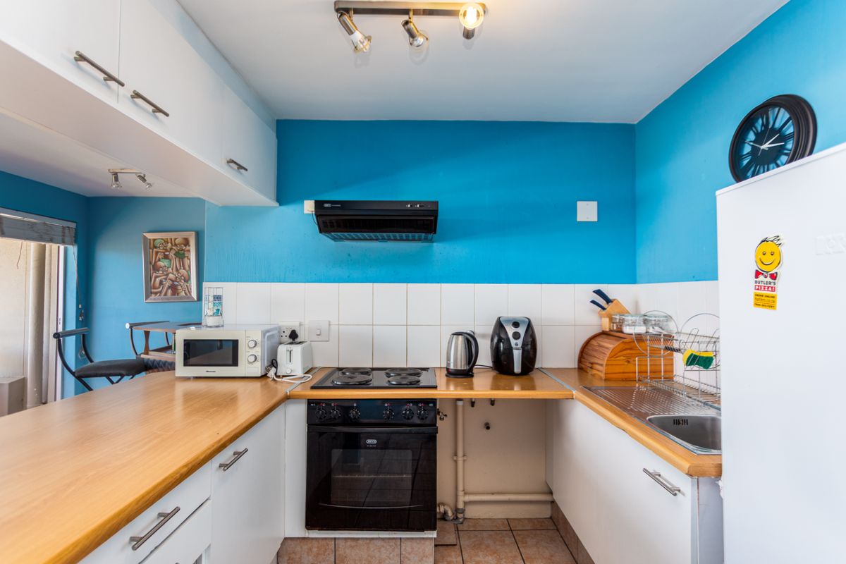 A functional kitchen featuring white cabinetry, wood-look countertops, a built-in oven with hob, and an extractor fan.