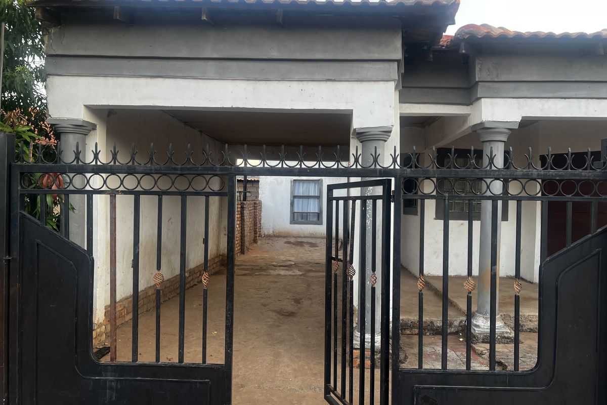 Front view of a residential property featuring a gated entrance, covered carport area, and traditional architectural columns.