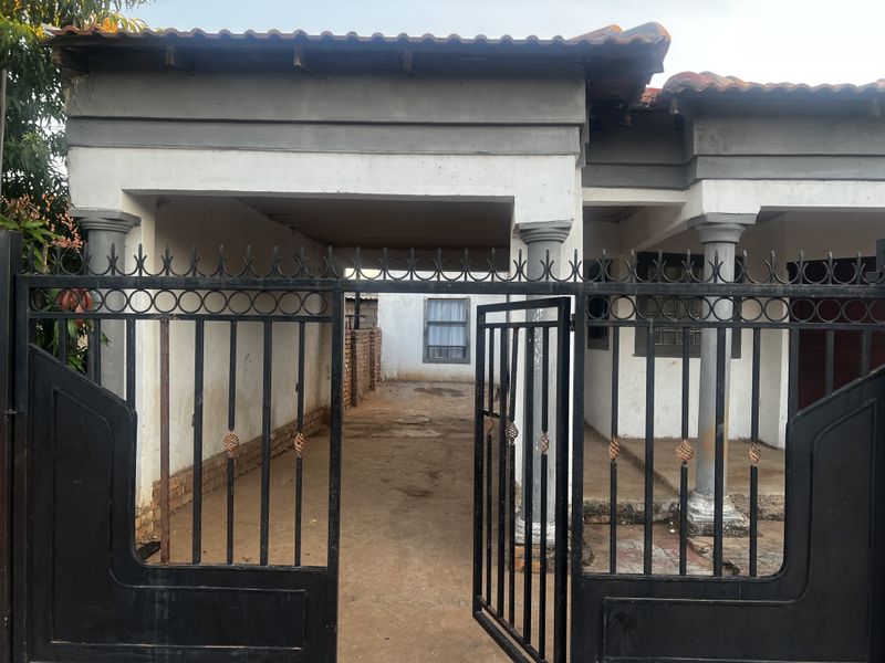 Front view of a residential property featuring a gated entrance, covered carport area, and traditional architectural columns.