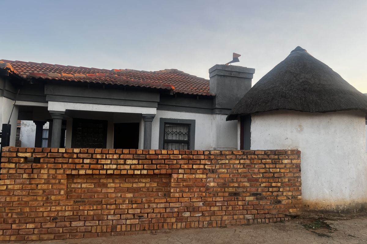 Front view of a house featuring a tiled roof section, a traditional thatched rondavel, and a face-brick boundary wall.