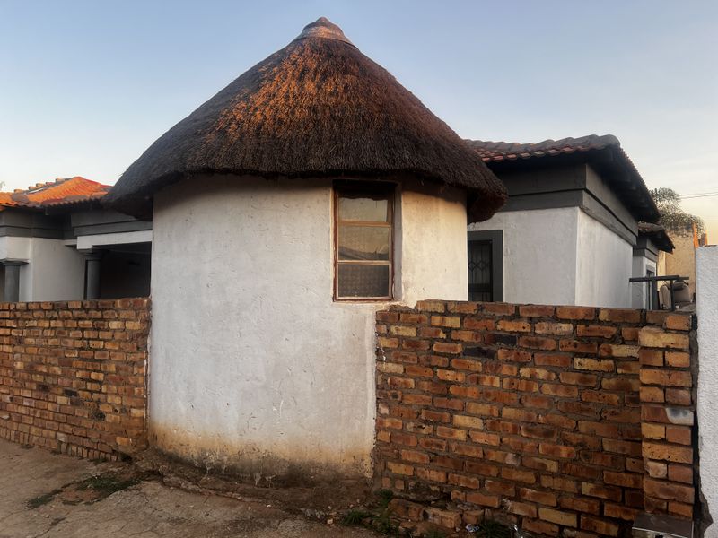 Exterior view of a house featuring a traditional thatched roof circular structure and a face-brick boundary wall.