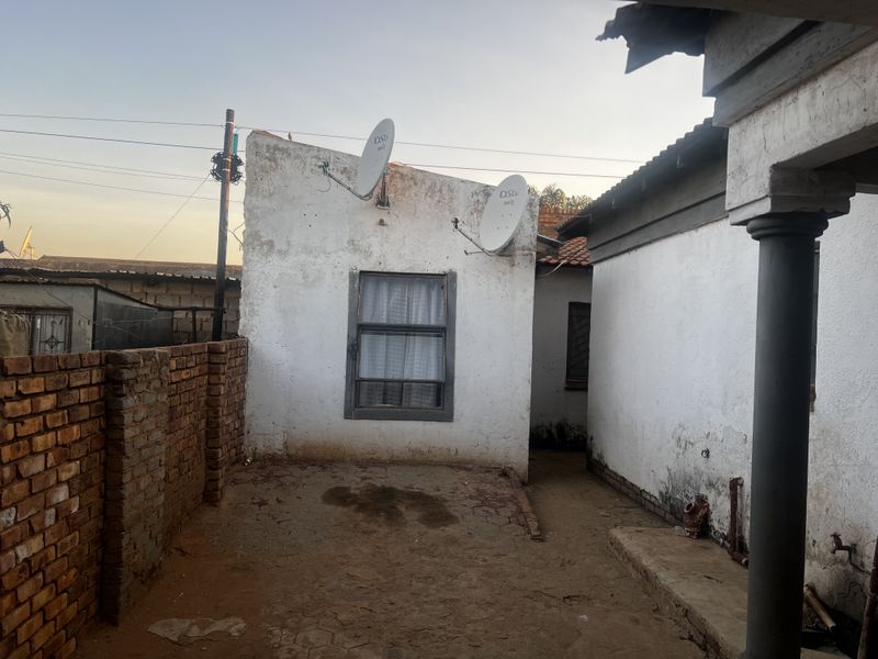 A view of the rear exterior area showing weathered brick and plastered walls, exposed ground, and satellite dish installations.