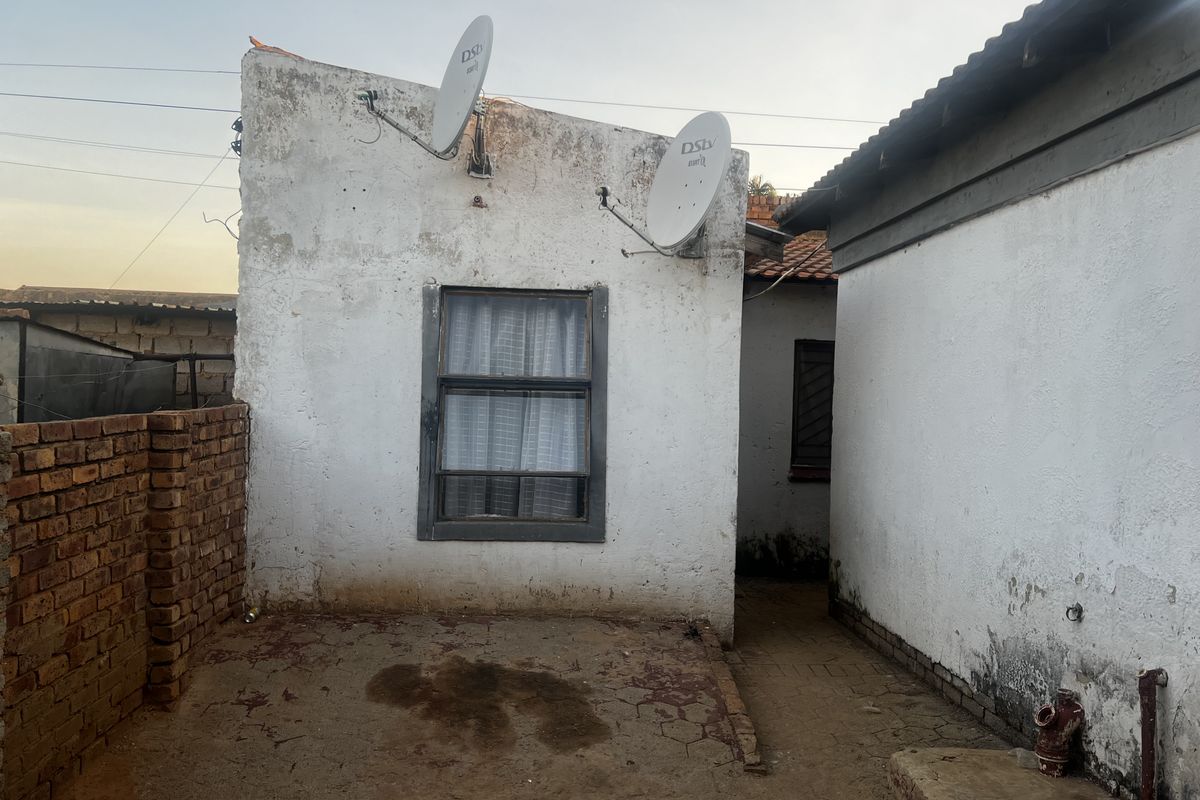 Rear exterior view of the property showing weathered walls, satellite dishes, and an unpaved courtyard area requiring maintenance.