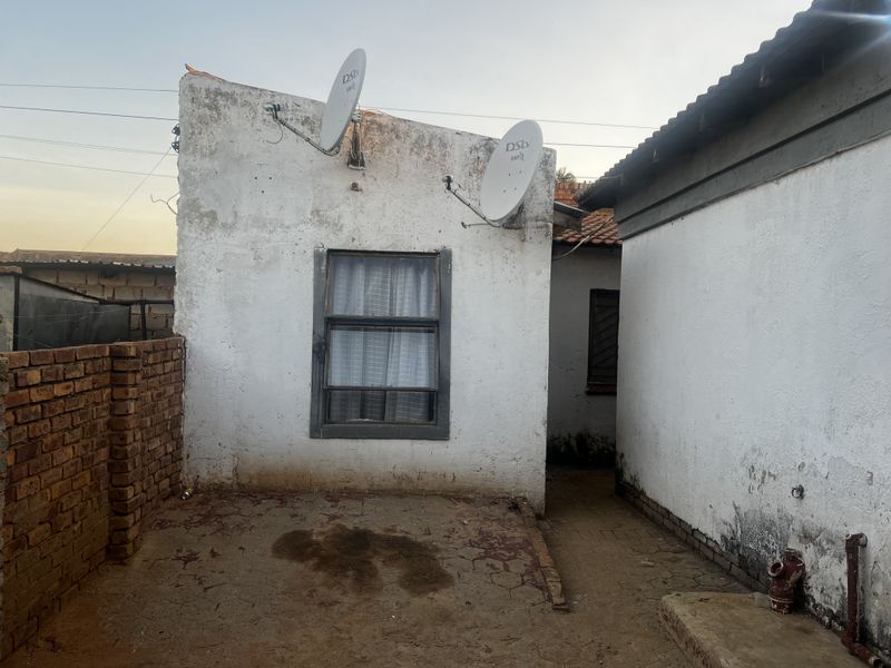 Rear exterior view of the property showing weathered walls, satellite dishes, and an unpaved courtyard area requiring maintenance.