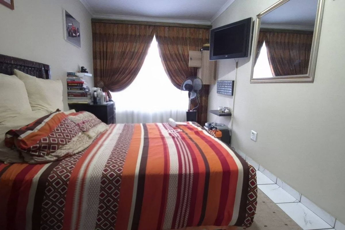 A standard bedroom featuring tiled flooring, neutral wall finishes, and a window with curtain treatments.