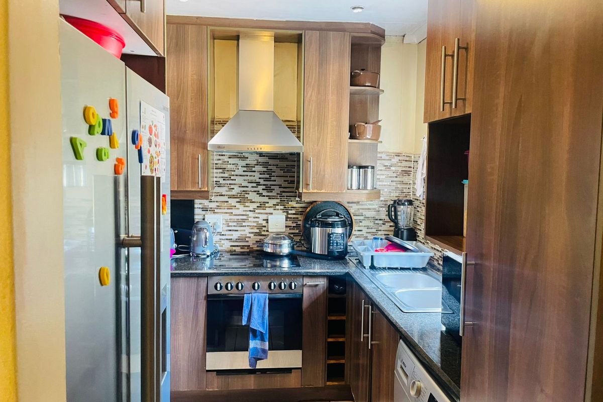 Compact galley-style kitchen featuring wood-finish cabinetry, granite countertops, stainless steel extractor fan, built-in oven, and tiled flooring.