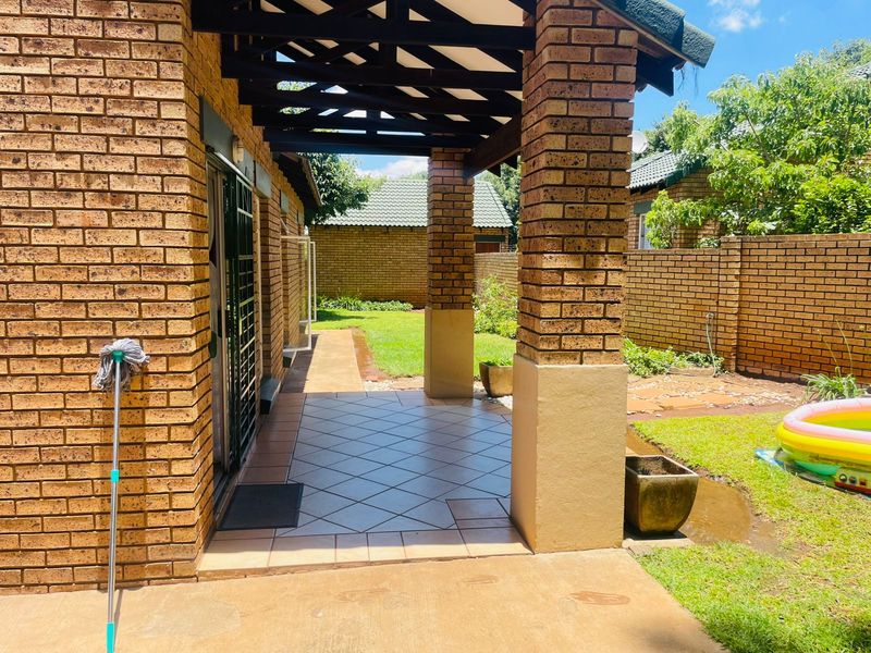 A covered patio area featuring face-brick pillars and tiled flooring, providing direct access to the rear garden and lawn.