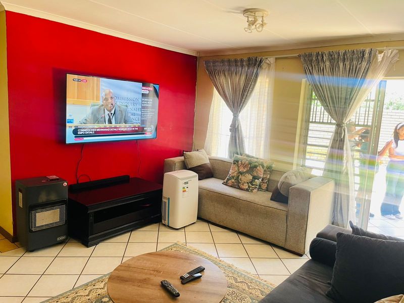 A living room featuring tiled flooring and a prominent red accent wall, with natural light entering through large windows.