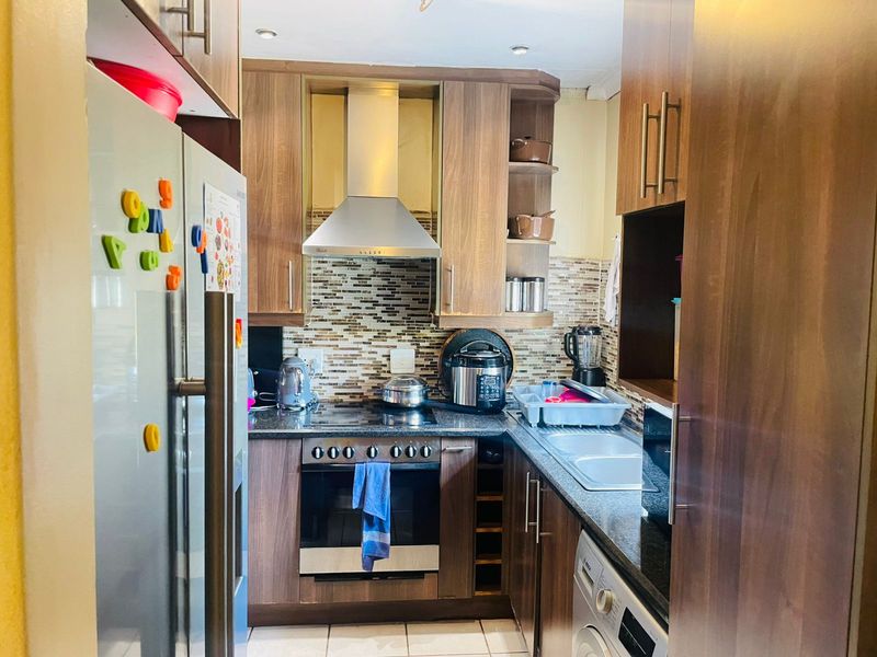 Compact galley-style kitchen featuring wood-finish cabinetry, granite countertops, stainless steel extractor fan, built-in oven, and tiled flooring.