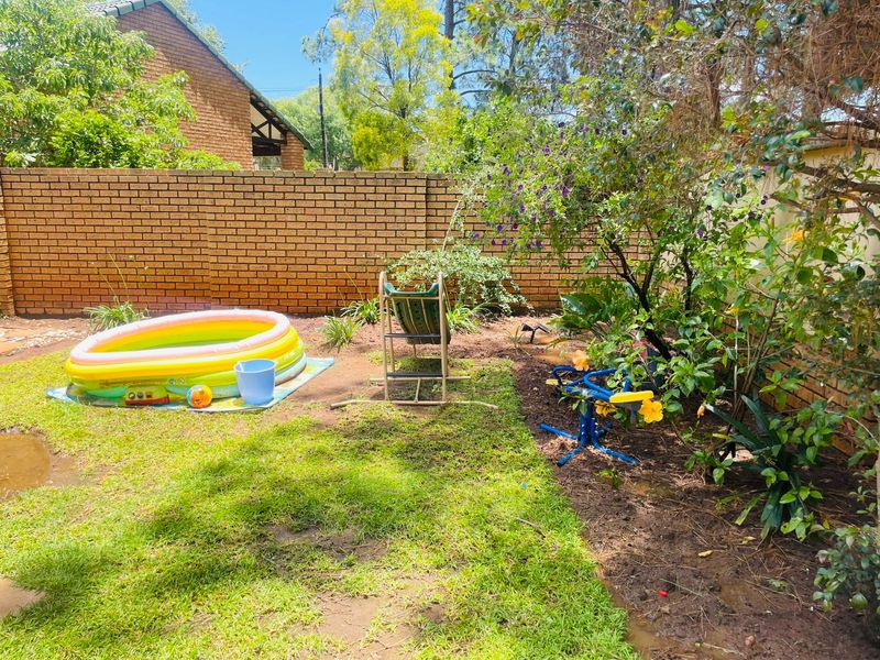 A private rear garden area featuring a brick boundary wall, established greenery, and a lawn space suitable for outdoor recreation.
