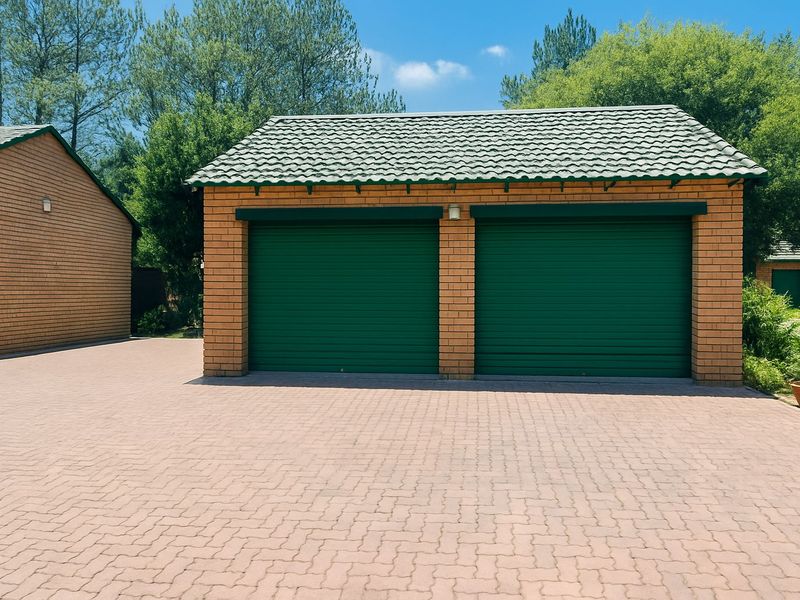 A double garage with green roller doors and a tiled roof, situated on a paved driveway.