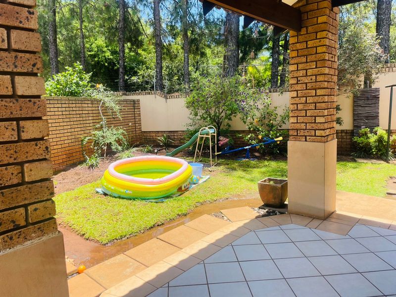 A covered patio overlooking a private garden with brick boundary walls and established trees.