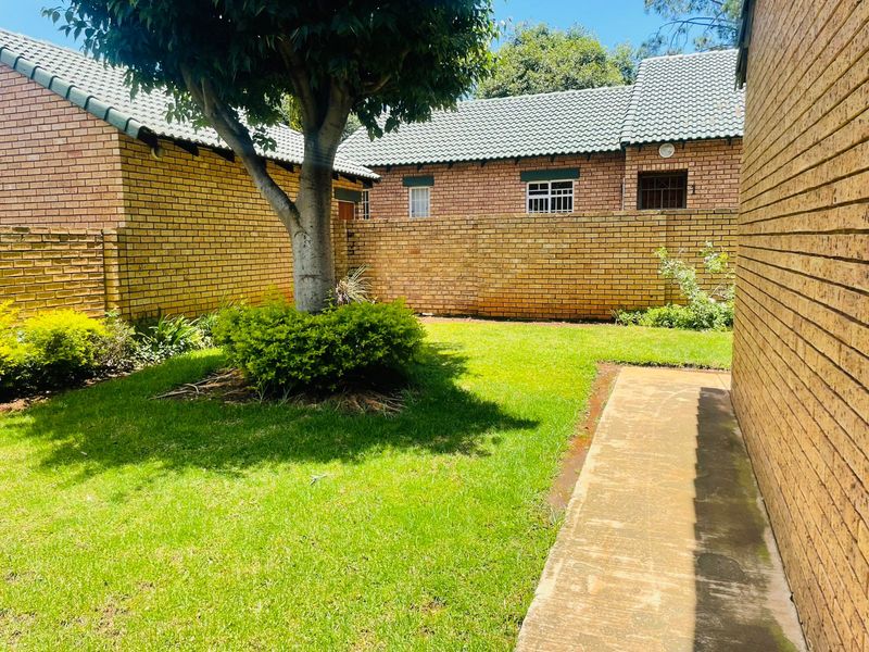 A private rear garden area featuring a well-maintained lawn, mature tree, and perimeter brick walling with a concrete pathway.