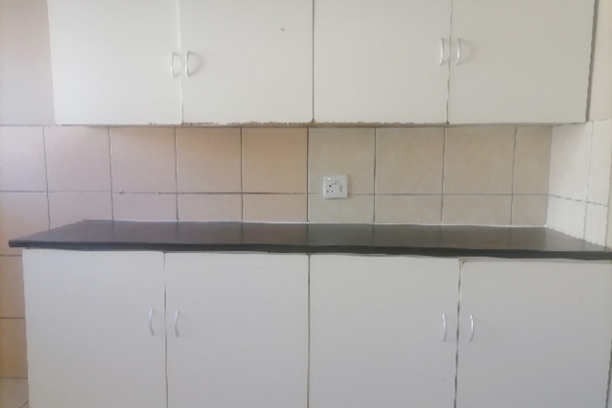 A functional kitchen area featuring white cabinetry, a dark countertop, and tiled splashback with an integrated electrical outlet.