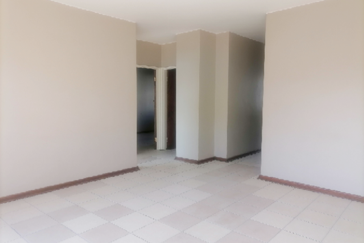 An empty, neutral-toned living area featuring tiled flooring and a clear transition into an adjacent room through a doorway.