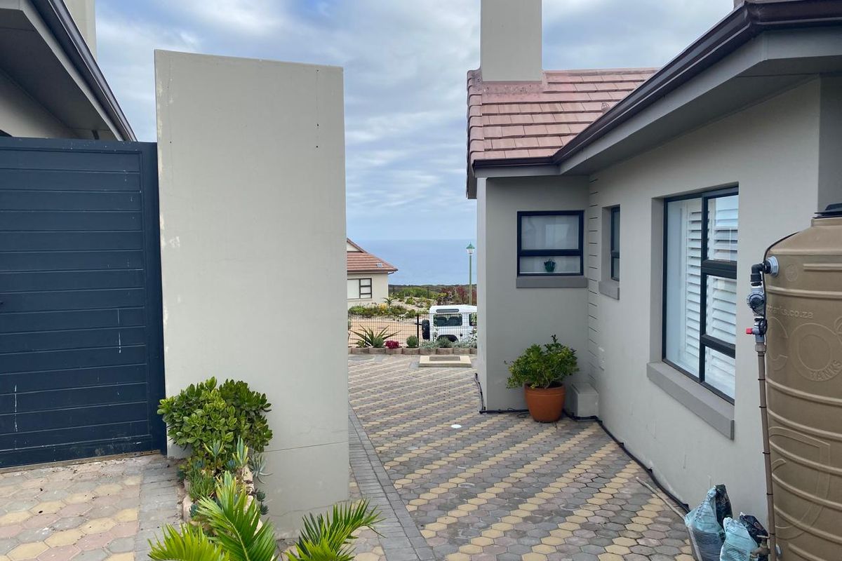 A paved side walkway between residential structures, featuring a water storage tank and views toward the coastline.